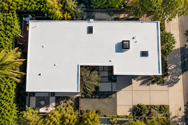 AI-generated illustration: pale membrane roof with perimeter coping on a mid-century home viewed from above